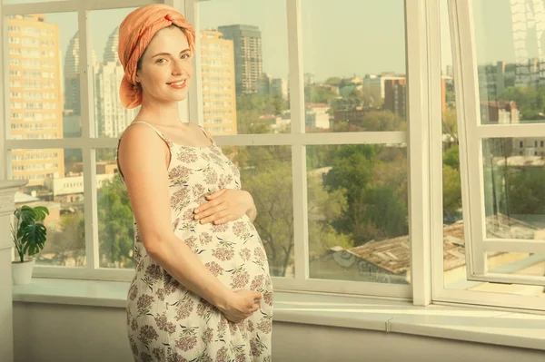 Красивая беременная женщина стоит у большого открытого окна — стоковое фото