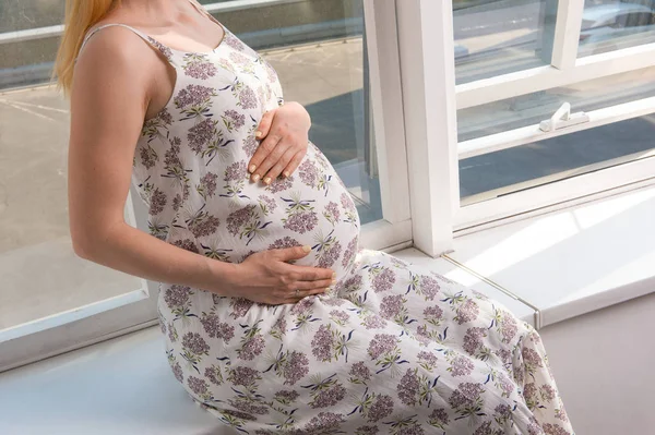 Nerozpoznatelný obrázek těhotné dívky sedící na okenní parapetu — Stock fotografie