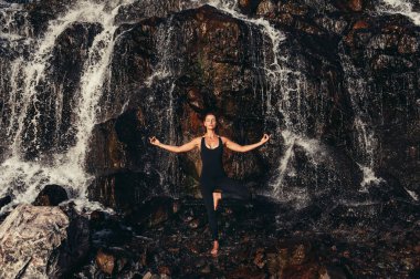 Güneş ışığında kayalık bir uçurumun yakınında yoga yapan sportif kadın