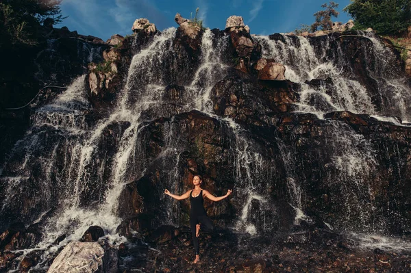 Frau praktiziert Yoga in der Nähe von Wasserfall beim Treffen am Morgen — Stockfoto