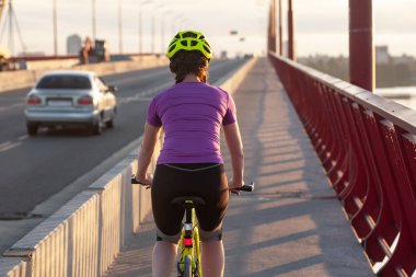 Gün batımında büyük köprüde ilerleyen kadın bisikletçi