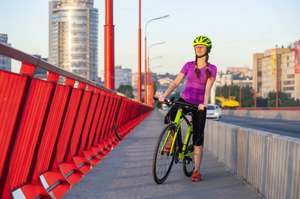 Активная девушка, стоящая на велосипеде с красивым городским видом на задний план — стоковое фото