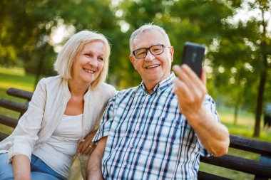 Kıdemli mutlu çiftimiz parkta smartphone kullanıyor.