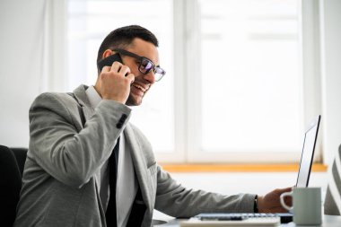 Mutlu genç işadamı ofisinde çalışıyor. 