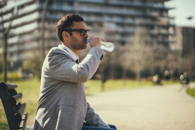Genç işadamı dinleniyor ve işten sonra parkta su içiyor.