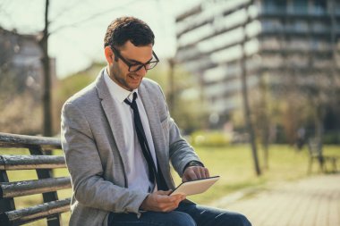 Genç mutlu işadamı parkta dijital tablet kullanıyor.