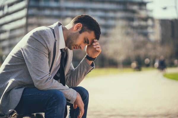 Young businessman is sitting in park after being fired. He is depressed.