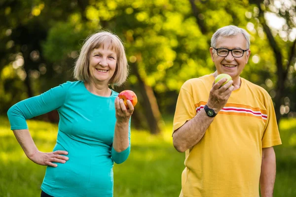 Happy senior couple is eating apples exercising in park.