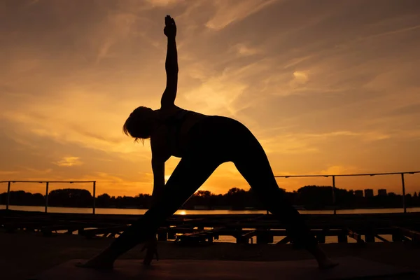 女人在日落时练习瑜伽 特里科纳萨纳 比克拉姆三角形左 — 图库照片