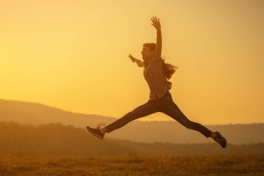 Mutlu çocuk gün batımında doğada zıplıyor.