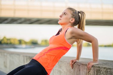 Genç bayan dışarıda egzersiz yapıyor. Ters şınav çekiyor..