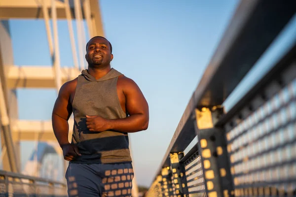 アフリカ系アメリカ人の若者が街の橋の上をジョギングしている — ストック写真