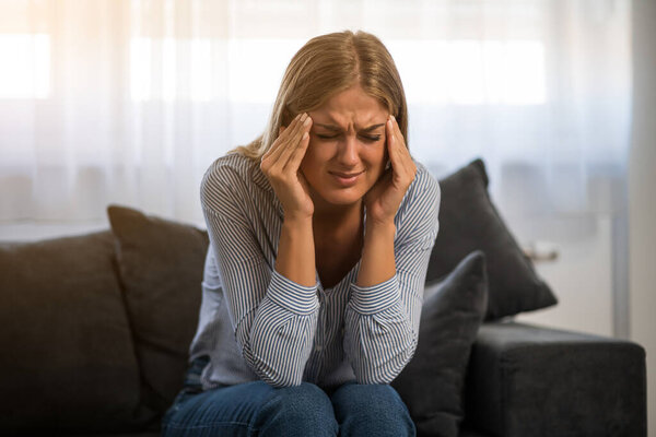 Молодая женщина устала после работы. Она сидит на диване и у нее болит голова..