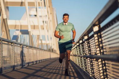 Genç mutlu adam şehirde köprüde koşuyor..