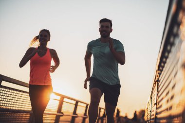 Genç çift gün batımında şehirde koşuyor..