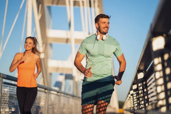 若い幸せなカップルが街の橋の上をジョギングしている — ストック写真