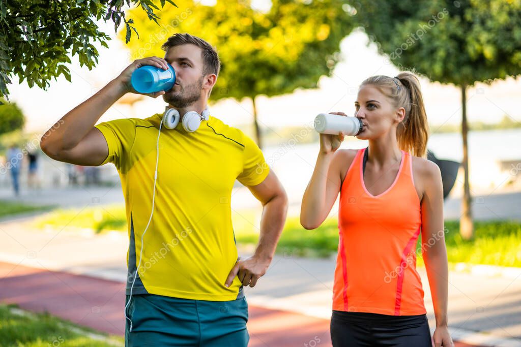 Young couple is drinking water while exercising outdoor.