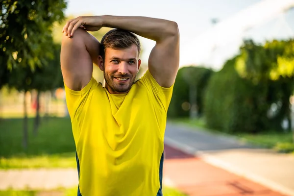 若い男が屋外で運動している 彼は体を伸ばしてジョギングのために暖まっている — ストック写真