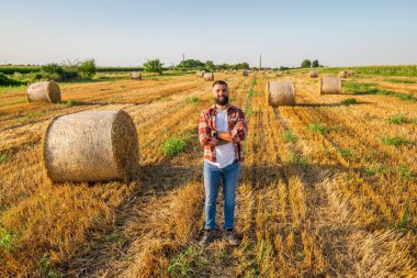 Çiftçi saman balyalarının yanında duruyor. O, başarılı bir hasattan sonra tatmin olur..