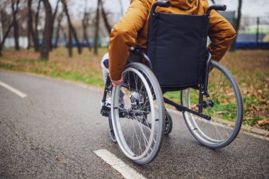 Parktaki tekerlekli sandalyedeki felçli sakat adamın yakın plan görüntüsü. Patikada yuvarlanıyor..