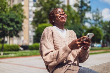 Genç mutlu siyah kadın akıllı telefon kullanıyor. Telefonla mesajlaşırken gülüyor..