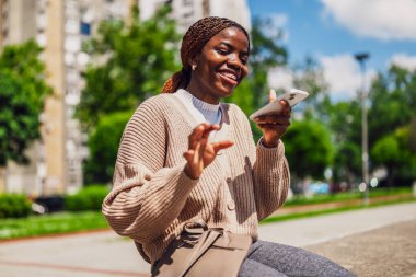 Genç mutlu siyah kadın akıllı telefon kullanıyor. Sesli mesaj kaydederken gülüyor..