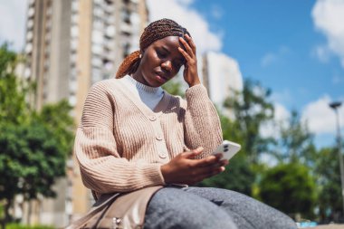 Genç siyahi kadın çevrimiçi mesajlaşma için akıllı telefon kullanırken çıldırmış durumda..