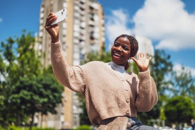 Genç mutlu siyah kadın akıllı telefon kullanıyor. Bir video görüşmesi yaparken gülüp el sallıyor..