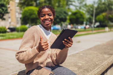 Çevrimiçi iletişim için dijital tablet kullanan neşeli bir zenci kadının portresi. İşten sonra dışarıda dinleniyor..