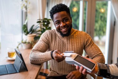 Rahat bir kafede otururken, günlük giysiler içindeki genç adam akıllı telefonuyla temas kurmadan ödeme yapıyor..