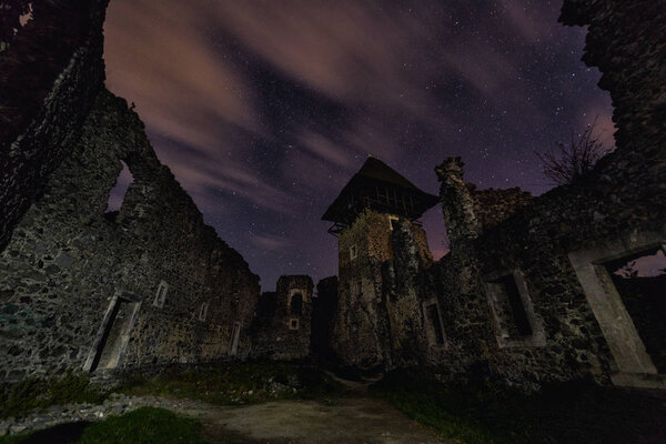 Ruins of medieval castle at night with amazing starry sky and clouds, mystical place, Nevytsky castle, Transcarpathia, Ukraine, Eastern Europe