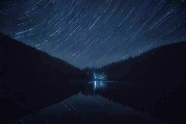 Night landscape with starry sky, star trails over the alpine lake Synevyr in Carpathian mountains, also known as sea eye of Carpathians, Ukraine