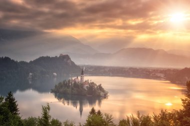 Popüler turizm lake Bled yumuşak sarı gündoğumu ışık ve bulutlu gökyüzü Meryem Varsayım hac kilise adada Alps dağlarla çevrili çarpıcı görünümü