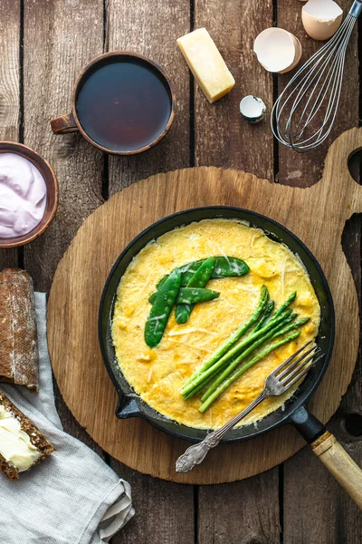 Omelet with green asparagus, pea on frying pan, top view, rustic style — Stock Photo, Image