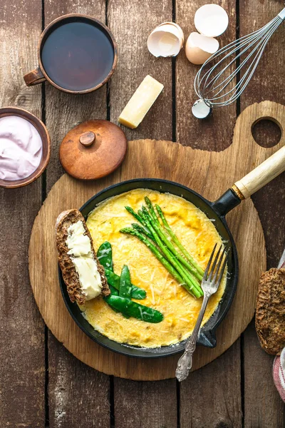 Omelet with green asparagus, pea on frying pan, top view, rustic style