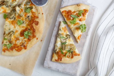 Enginar ve roka kesme tahtası üzerinde peynir pizza