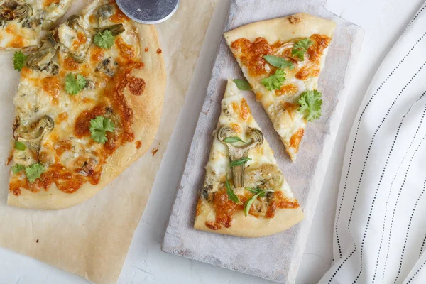 Enginar ve roka kesme tahtası üzerinde peynir pizza