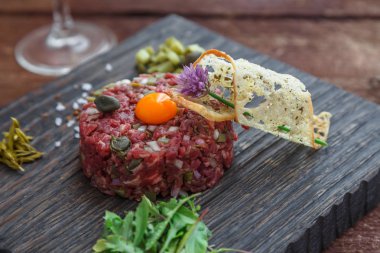 Biftek tartare kapari, salatalık turşusu ve koyu arka plan üzerinde taze soğan ile