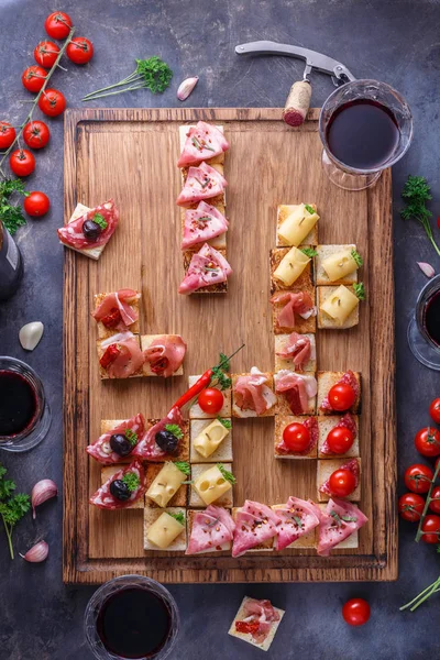 Appetizers table with italian antipasti snacks and wine in glasses. Brushetta or authentic traditional spanish tapas set, cheese variety board over grey concrete background. Top view, flat lay