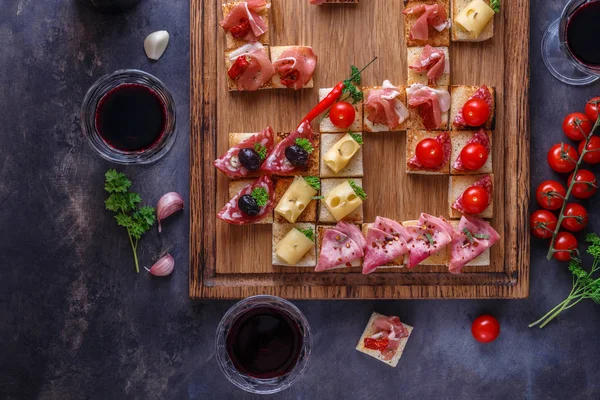 Appetizers table with italian antipasti snacks and wine in glasses. Brushetta or authentic traditional spanish tapas set, cheese variety board over grey concrete background. Top view, flat lay