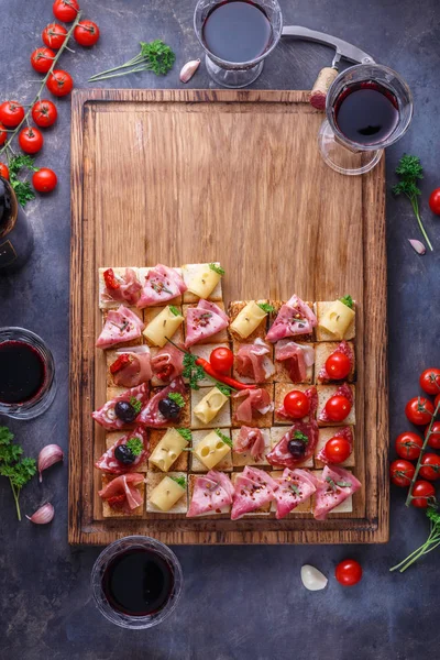 Gustosi antipasti salati di pomodoro italiano, o bruschette, fette di baguette tostate condite con prosciutto, prosciutto su un tagliere di legno — Foto Stock