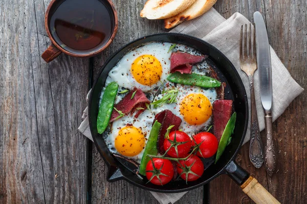 Huevos fritos en una sartén con tomates cherry, guisantes verdes y pastrami. Espacio de copia —  Fotos de Stock