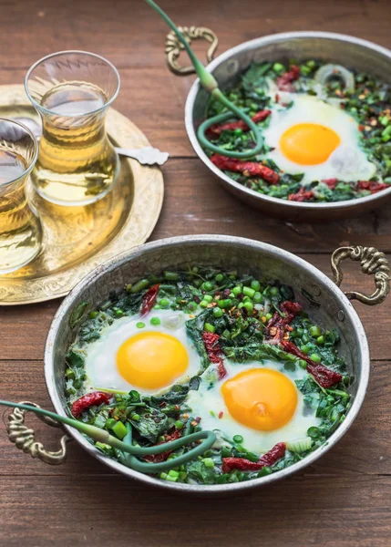 Shakshuka verde. Huevos fritos con espinacas frescas, ramson, puerro en una sartén sobre un fondo gris, vista superior —  Fotos de Stock