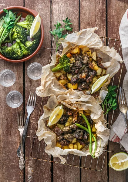 Kleftiko grego tradicional, um guisado de cordeiro assado no forno com batata, azeite, cebola, cenoura, alho e ervas, servido com limão e ouzo . — Fotografia de Stock