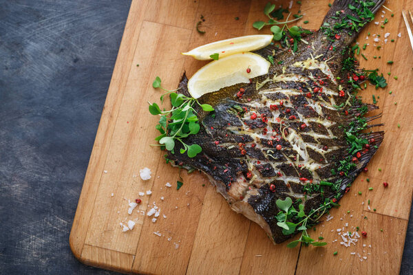 Запечённая камбала с лимоном на деревянной доске, место для копирования
