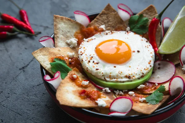Desayuno mexicano: chilaquiles con huevo, aguacate y verduras de cerca en un plato —  Fotos de Stock
