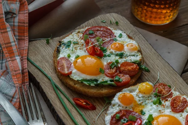 Fried eggs and tomato toasts on wooden cutting board — Stock Photo, Image