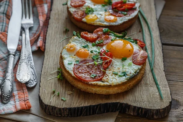 Sunny side fried eggs with tomato and bread on cutting board
