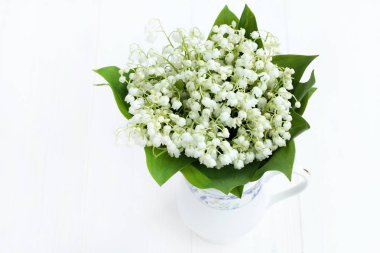 güzel beyaz boyalı ahşap masa üzerinde beyaz sürahi içinde vadideki zambak buketi