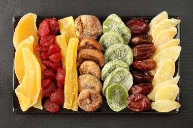 Mango, papaya, kivi, Kuru Meyve parçaları; kurutulmuş çilek, incir, tarihler; adet siyah seramik tabak siyah bir taş yüzey içinde yatan şekerlenmiş zencefil kökü. Makro